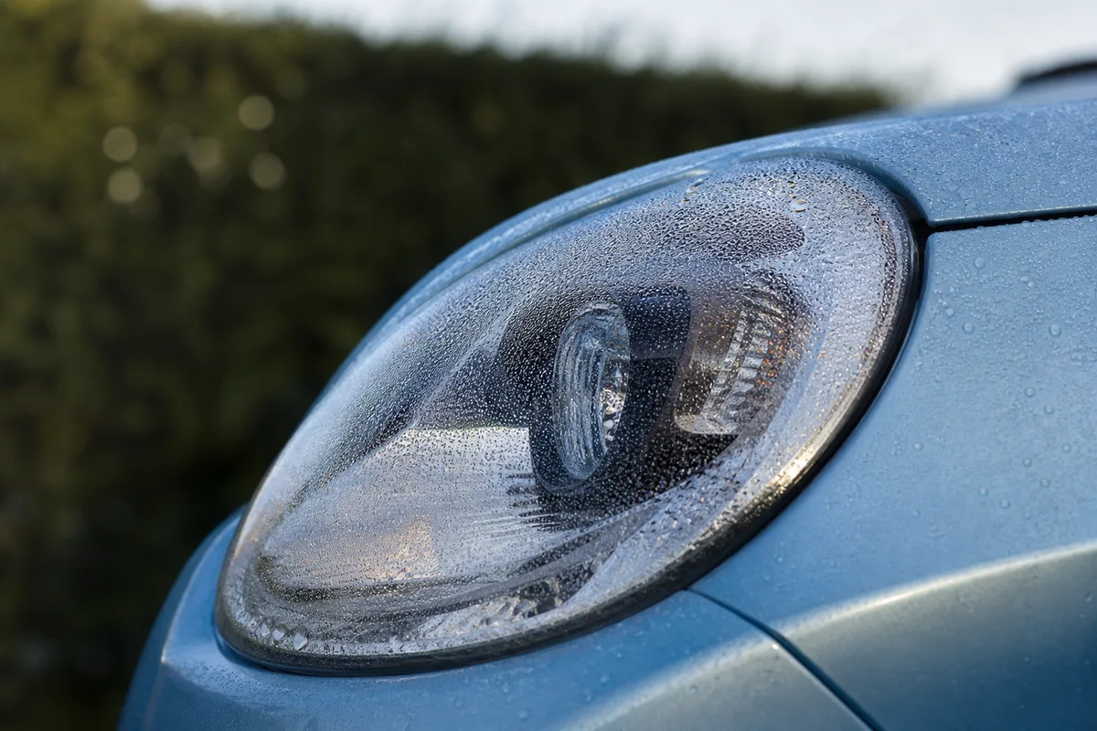 Gros plan sur l&rsquo;optique de phare avant d&rsquo;une voiture compacte couverte de rosée au petit matin