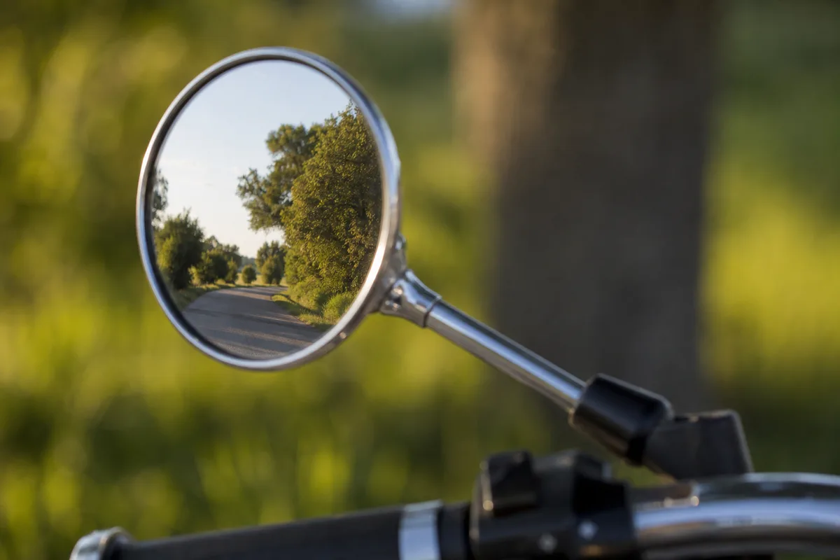 Rétroviseur de moto reflétant une route de campagne bordée d’arbres