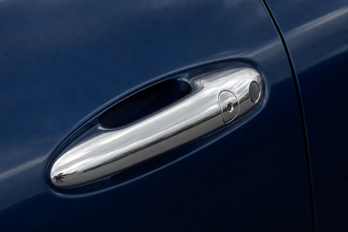 Poignée de portière chromée en gros plan sur une carrosserie bleu foncé, reflets de lumière