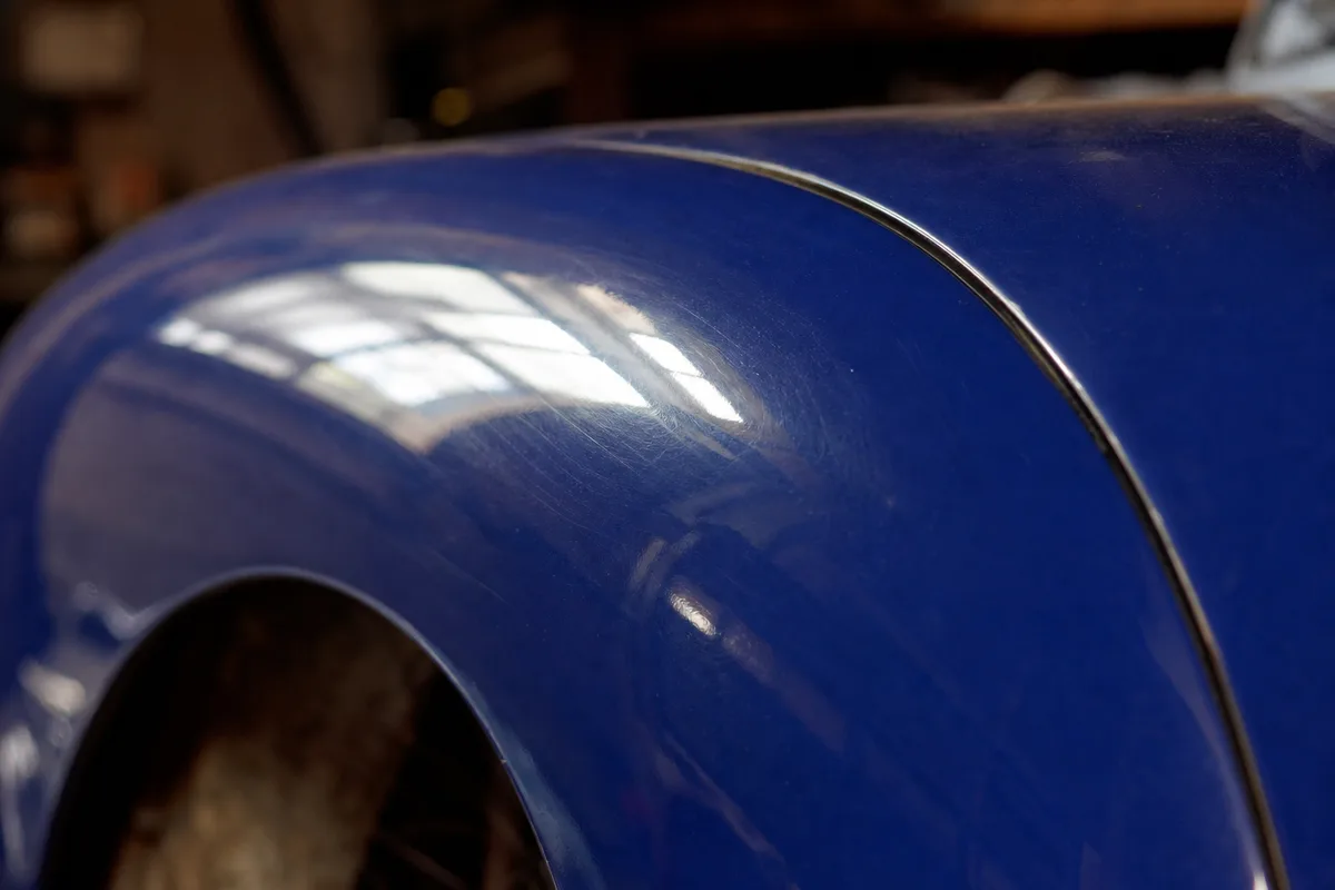 Aile avant d’une automobile ancienne en carrosserie bleue polie, vue rapprochée dans un atelier