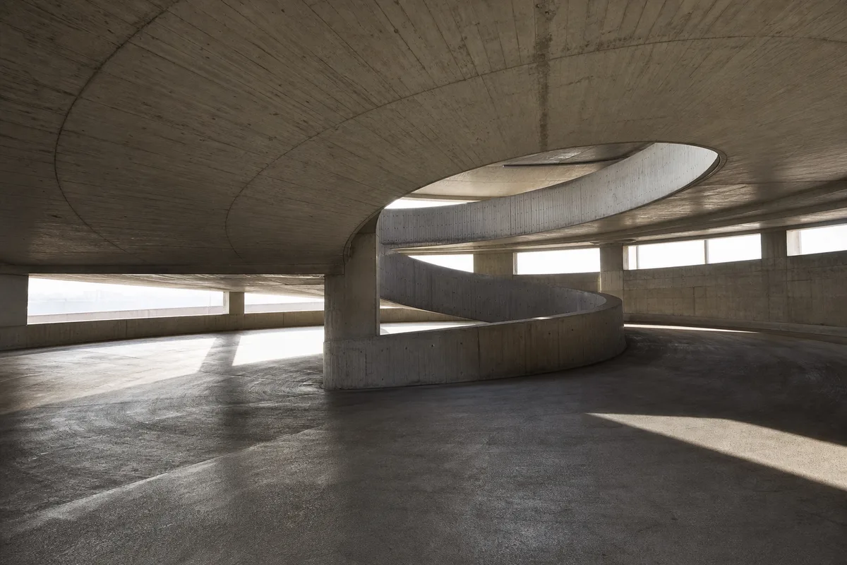 Rampe hélicoïdale d’un parking en béton brut entièrement vide, lumière matinale rasante