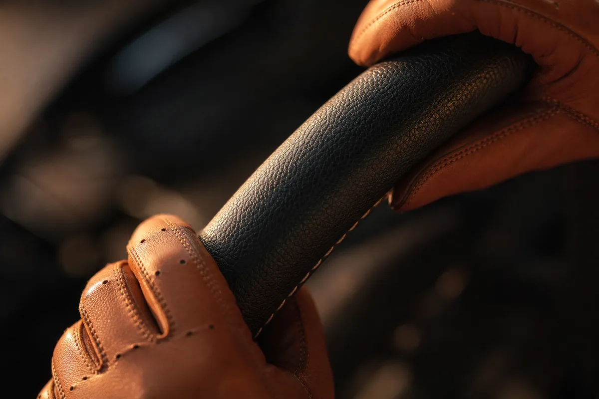 Mains gantées de cuir posées en haut de la jante d&rsquo;un volant, cadrage serré vu du dessus