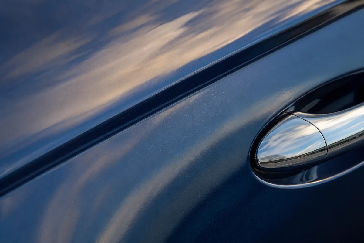 Détail de carrosserie d’une berline bleu nuit, poignée de portière chromée et reflets du ciel