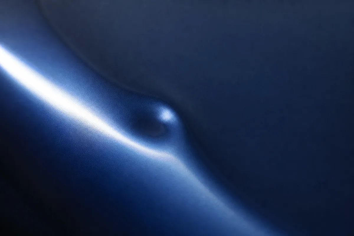 Gros plan sur une ondulation de tôle laquée bleu nuit, lumière rasante révélant un léger enfoncement