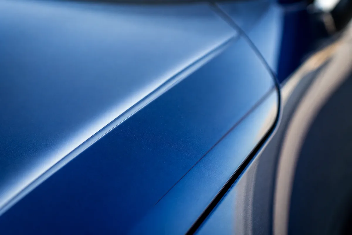 Détail macro d’une carrosserie bleu métallisé, nervure de capot et jonction d’aile