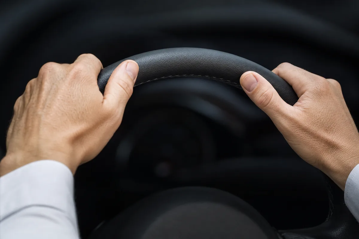 Mains posées sur le volant d&rsquo;une voiture, cadrage serré, habitacle sombre et lumière naturelle diffuse