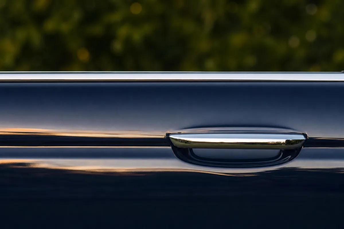 Détail d’une portière de voiture sombre et de sa poignée chromée sous une lumière rasante de fin de journée