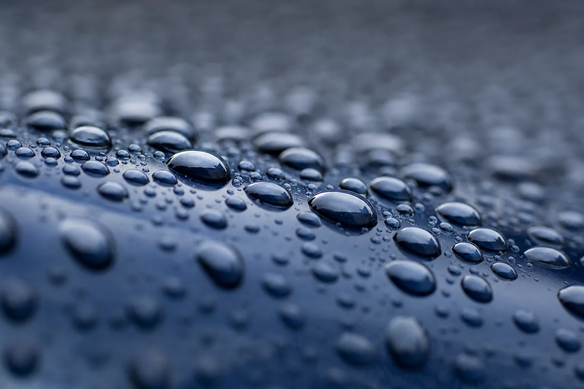 Gouttes de pluie sur une carrosserie bleu nuit en macro, reflets abstraits et faible profondeur de champ