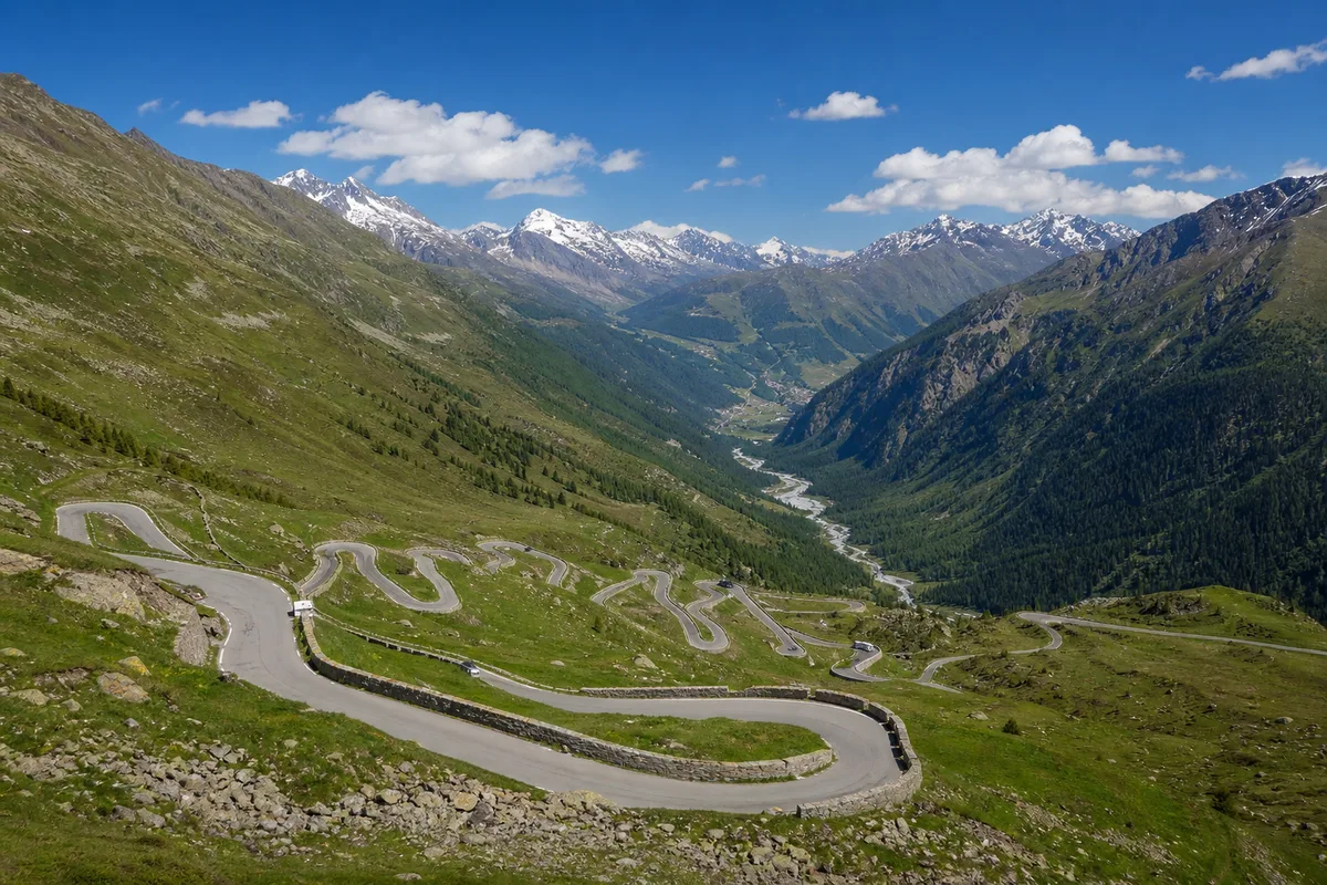 Route de col alpin en lacets vue depuis un belvédère, versants verts et sommets enneigés