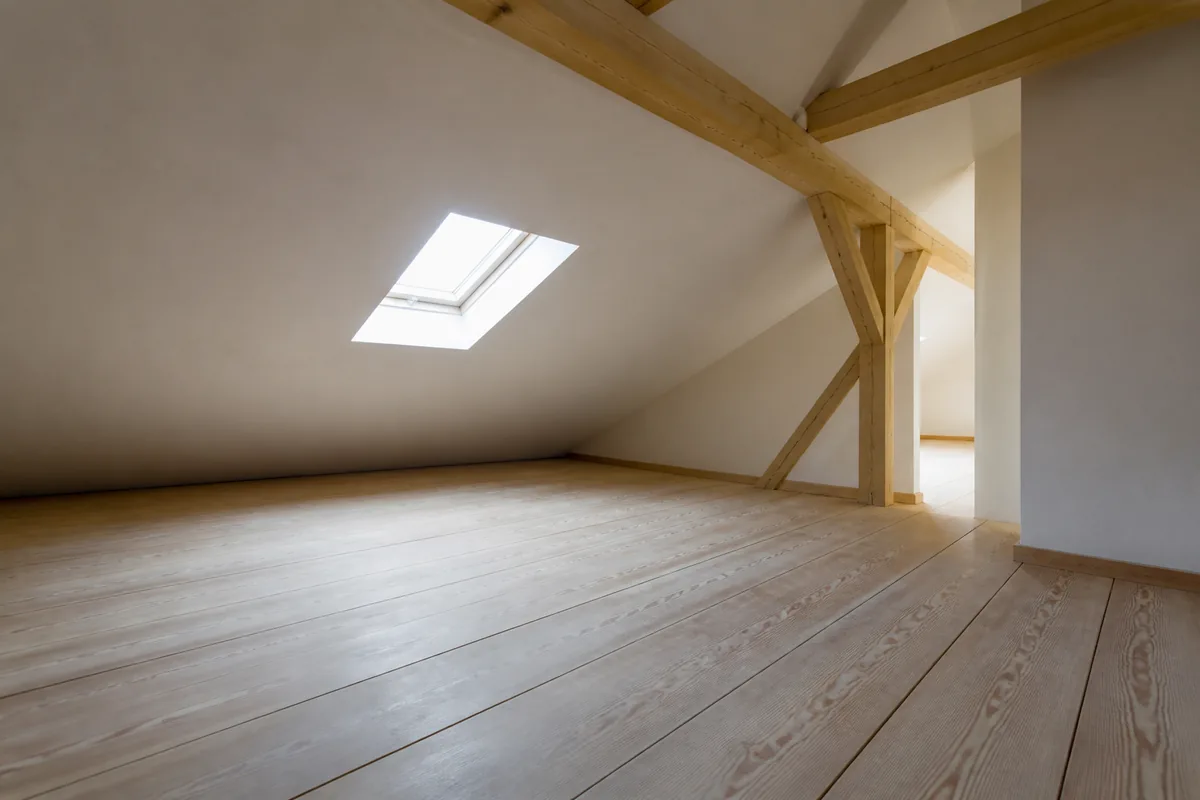 Comble aménagé sous charpente en bois clair avec rampant descendant vers un plancher en lattes